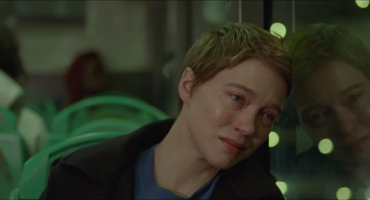 One Fine Morning (2022) movie still: closeup — The interior of a public bus at night with green plastic seats. A young woman with short hair presses…