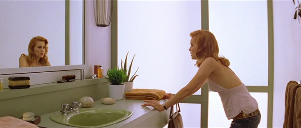 Where The Truth Lies (2005) movie still: medium — A light-colored bathroom features a green basin and frosted glass panels on the wall. A woman…