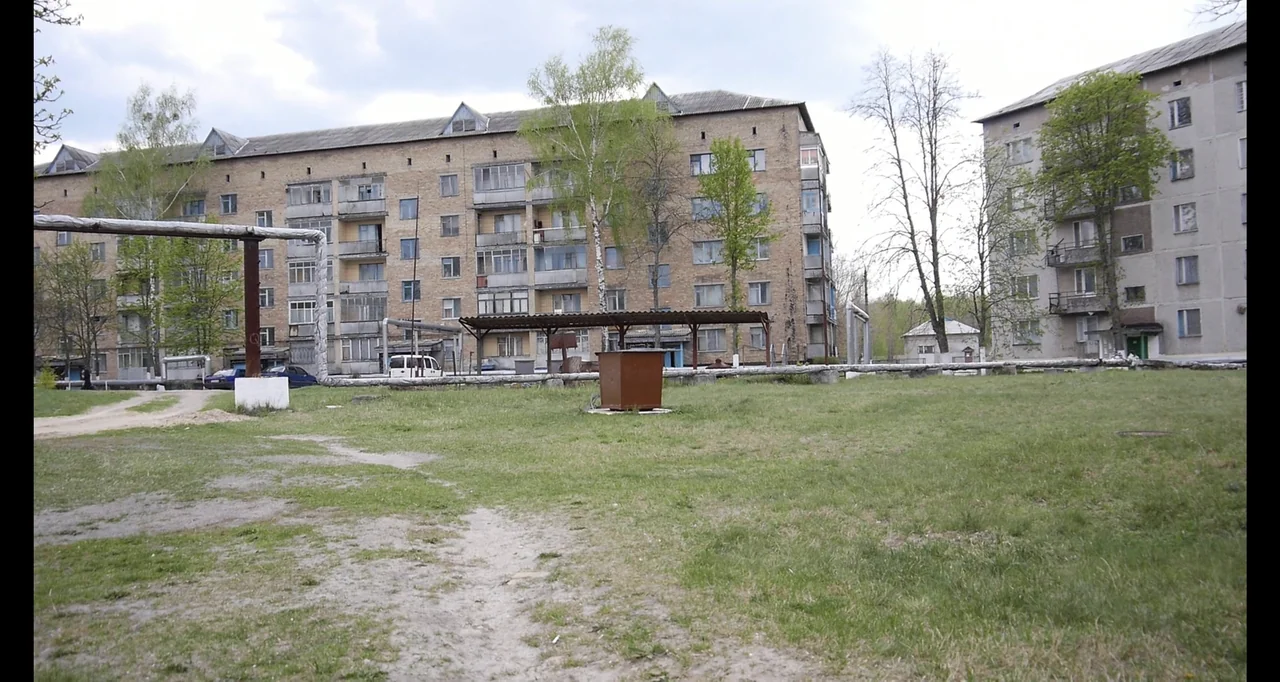 Chernobyl's Café (2016) movie still: wide — An exterior view of Soviet-style residential brick apartment blocks surrounding a grassy courtyard area.…