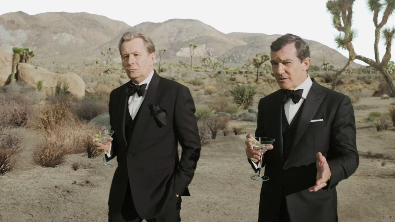 The Laundromat (2019) movie still: medium — Two men stand in a vast, arid desert landscape dotted with Joshua trees and mountains. They are wearing…