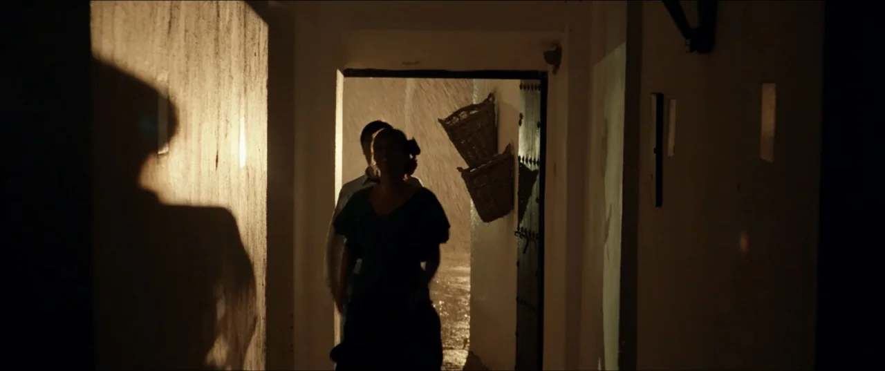 Hear Me: Our Summer (2024) movie still: medium — A dark corridor leads to an exterior doorway where heavy rain is visible outside. A man and a woman…