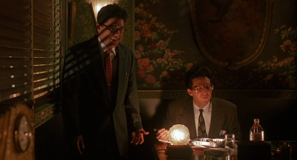 Mo’ Better Blues (1990) movie still: medium — A dark booth in a restaurant features floral wallpaper and slatted window blinds. Two men in suits…
