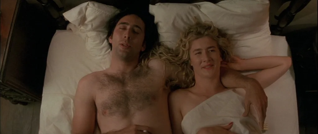 Wild At Heart (1990) movie still: medium — A man and woman lie together on a white sheet in a dark room. The view is from directly above the two…