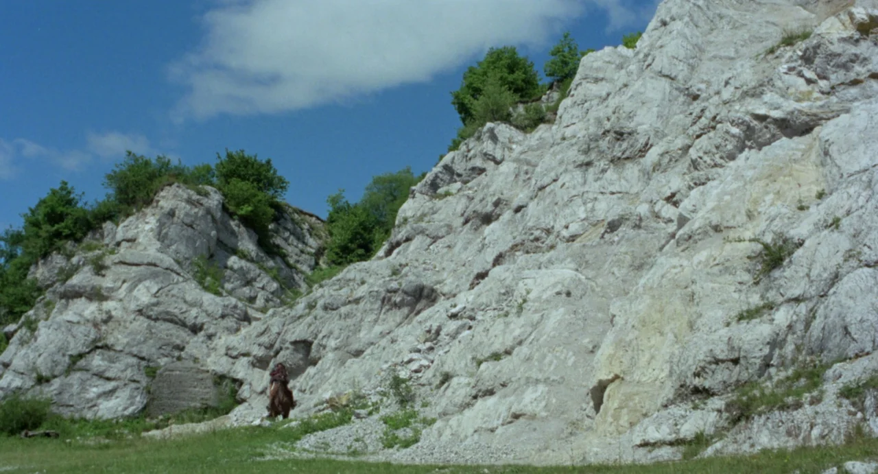 Johnny Colt (1966) movie still: wide — A tall, jagged limestone quarry wall dominates the scene under a bright sky. A lone figure on horseback…