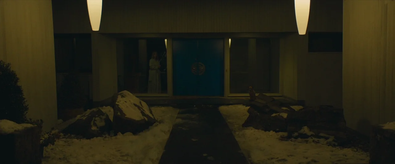 A Most Violent Year (2014) movie still: wide — A modern house exterior at night features a blue door and snowy landscaping. A woman observes from…