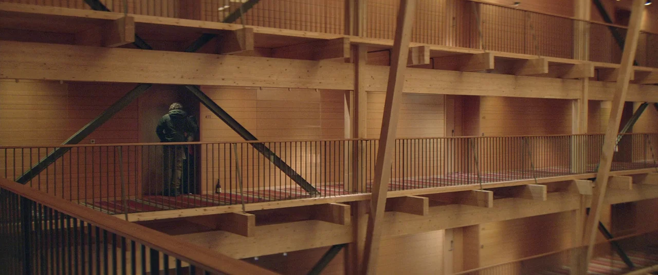 Force Majeure (2014) movie still: wide — A modern multi-level building features timber beams and structured wooden walls. A lone figure in a dark…