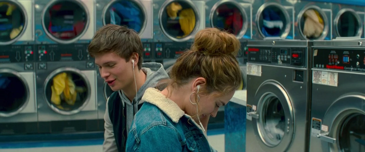 Baby Driver (2017) movie still: medium — Rows of stainless steel commercial washers fill a brightly lit public facility. A young man and woman stand…
