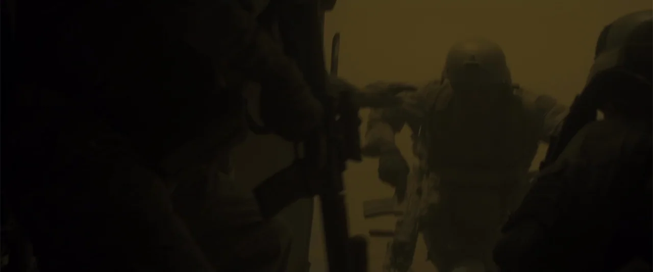 American Sniper (2014) movie still: medium — Three soldiers advance through a dense cloud of golden dust in an arid environment. Each figure carries…