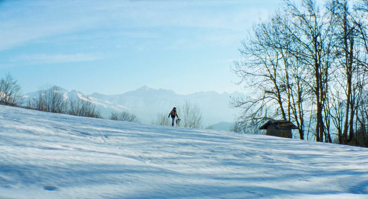 Anatomy of a Fall (2023) movie still: wide — A wide, snow-covered mountain landscape features a small stone hut and bare trees. A lone individual…