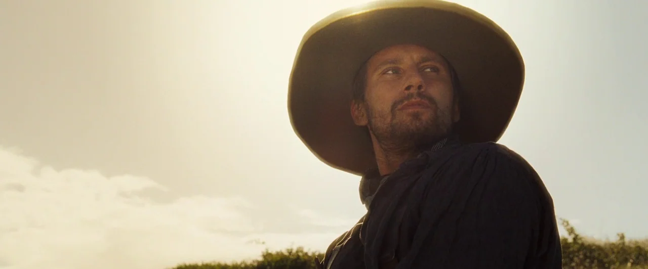 Far from the Madding Crowd (2015) movie still: medium — An open rural landscape is filled with bright, hazy sunlight behind a lone man. The man…
