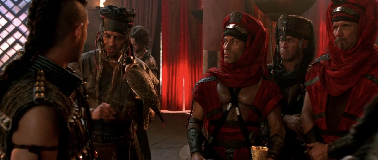 The Scorpion King (2002) movie still: medium — A dimly lit desert tent features red drapery and warm firelight. Several men wearing ornate red…