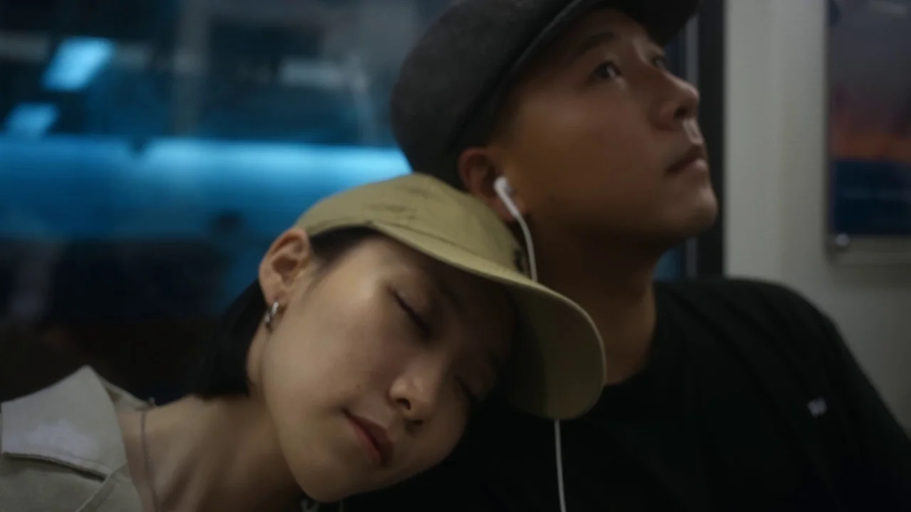 The Last Year of Darkness (2023) movie still: closeup — The interior of a dimly lit subway car at night features muted blue tones. A young woman…