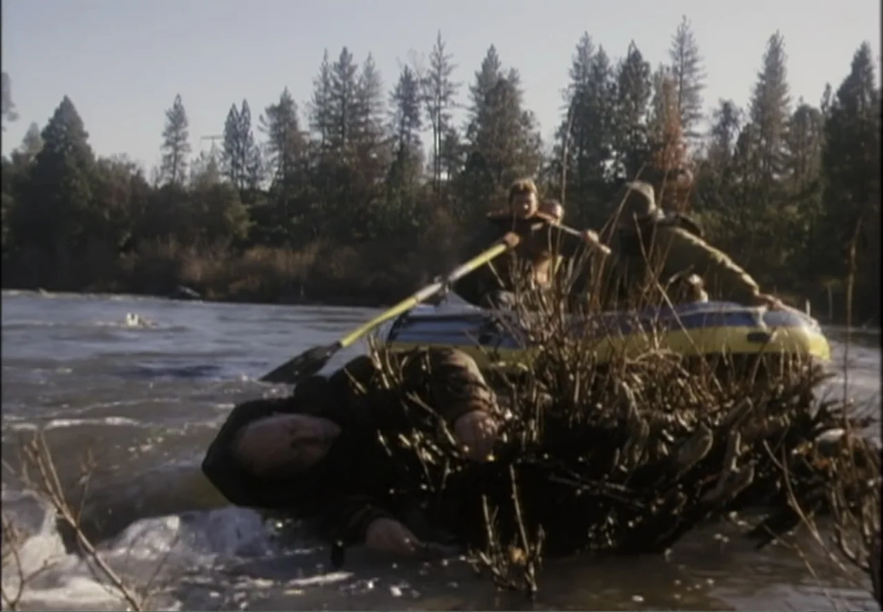 White Mile (1994) movie still: wide — A group of men in a raft navigate through turbulent river waters near a bank. The men struggle to steer the…