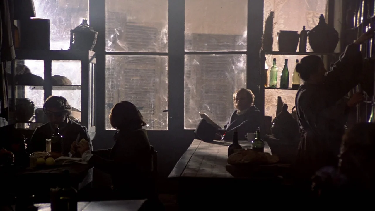 The Duellists (1977) movie still: medium — A rustic tavern interior has dark wooden furniture and rows of glass bottles on shelves. Several people…