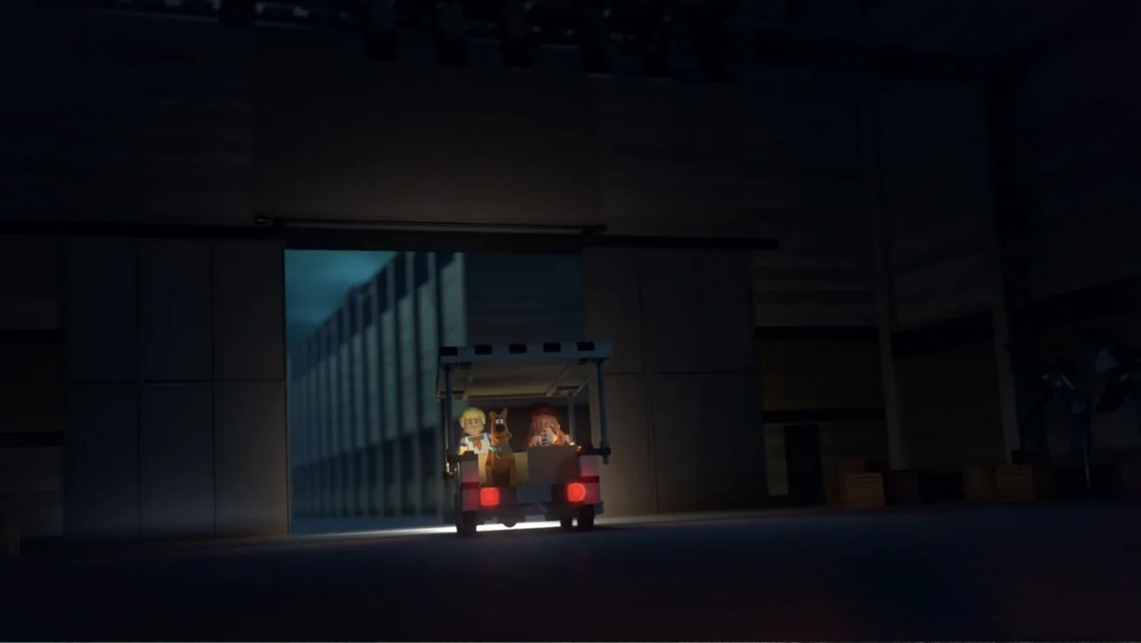 LEGO Scooby-Doo! Haunted Hollywood (2016) movie still: wide — A dimly lit industrial space with a large sliding door open to the night. A small toy…
