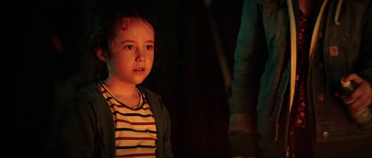 The Boogeyman (2023) movie still: medium — A dark, dimly lit environment where a young child is observed at close range. An adult arm enters the…