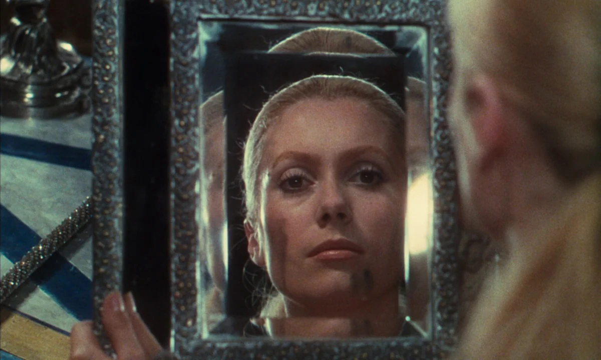 Donkey Skin (1970) movie still: closeup — A woman looks at her reflection in a small, ornate, rectangular hand-held mirror. The frame is silver with…