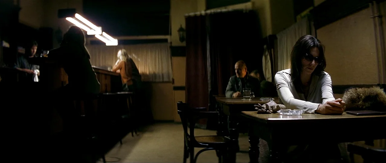 The Lives of Others (2006) movie still: wide — A dimly lit pub with dark wooden furniture and beige walls in shadow. A woman sits alone at a table…