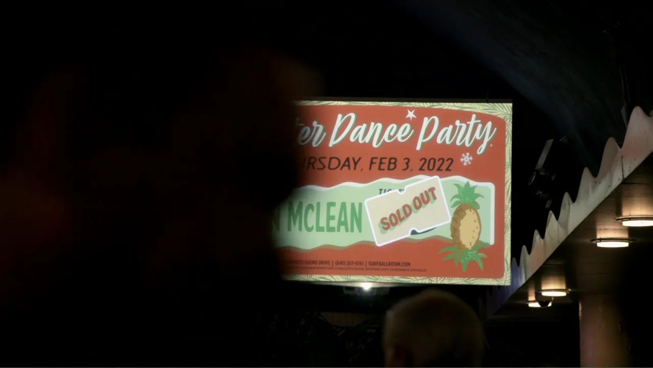 The Day the Music Died: The Story of Don McLean's "American Pie" (2022) movie still: medium — An exterior night view shows a bright, illuminated…