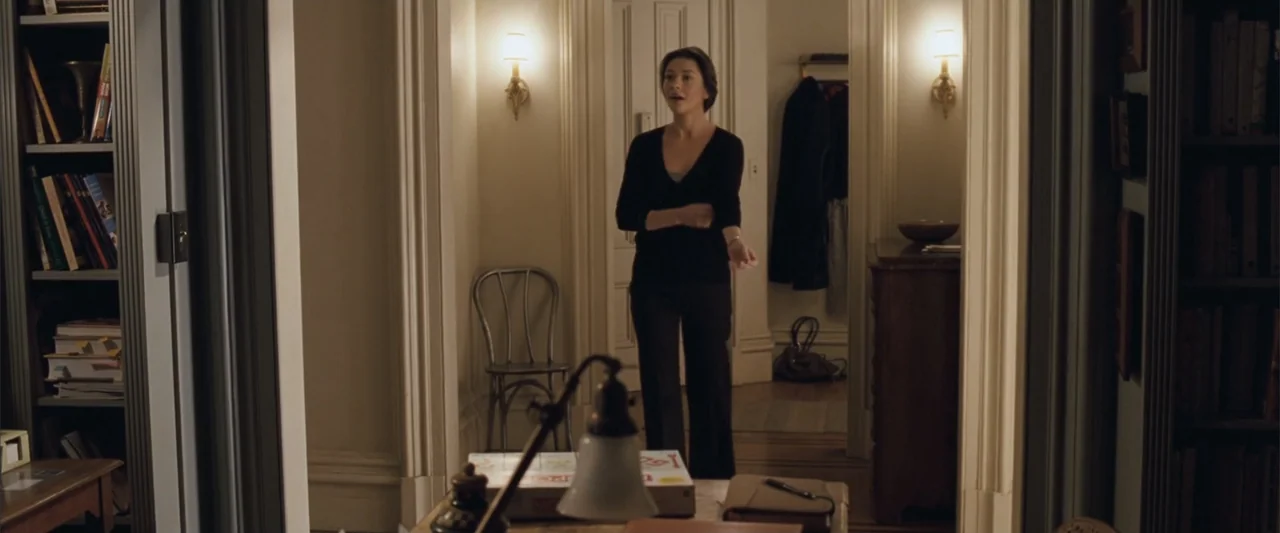 No Reservations (2007) movie still: medium — An apartment hallway with white door frames and built-in bookshelves on either side. A woman in a black…
