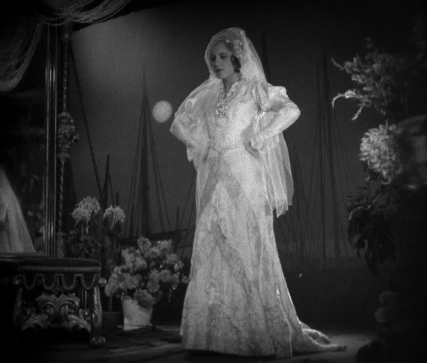 The Threepenny Opera (1931) movie still: fullbody — A stylized interior space features a woman in a formal white lace wedding gown. She stands in…