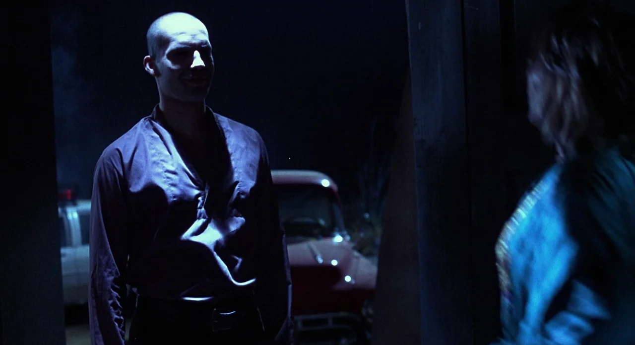 Tales from the Crypt: Demon Knight (1995) movie still: medium — A dark outdoor space at night featuring a parked red vintage car visible behind. A…