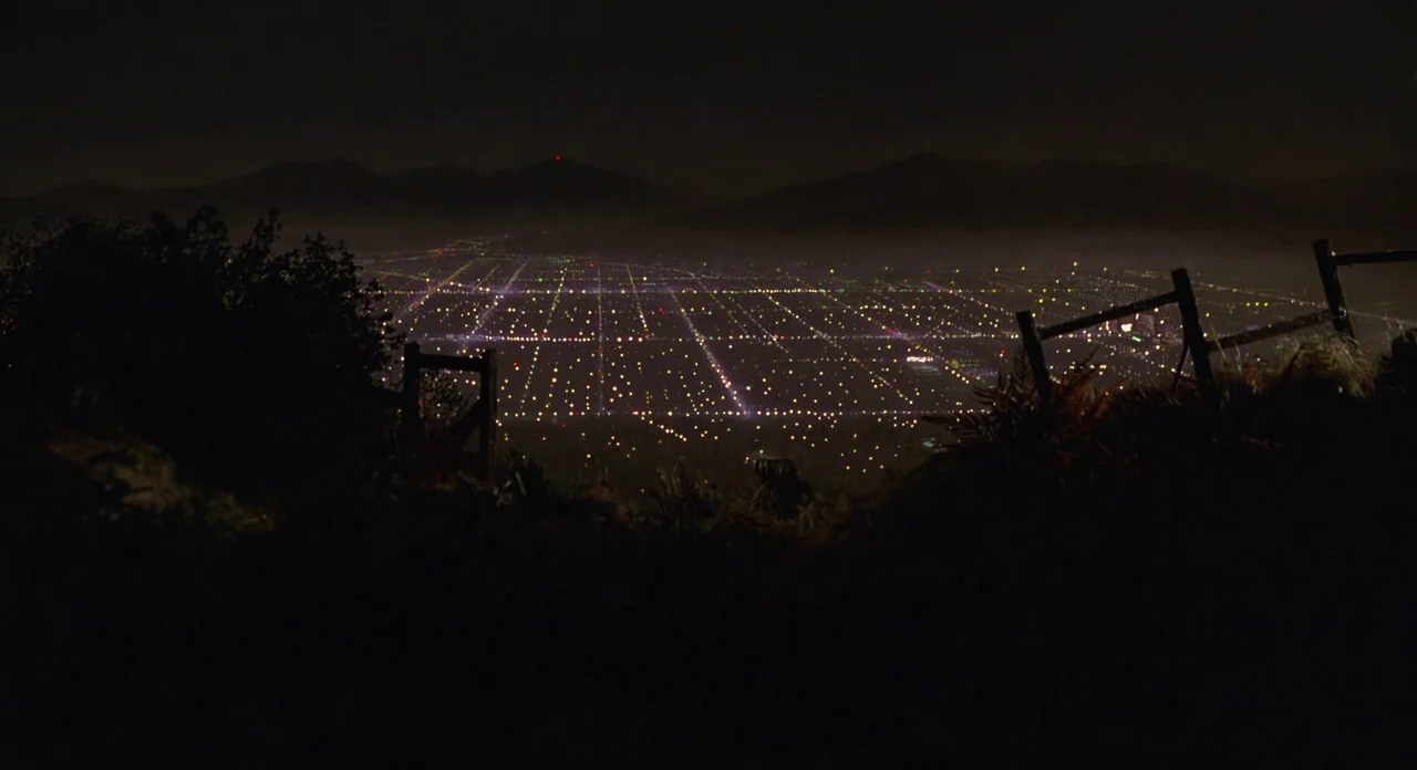 E.T. The Extra-Terrestrial (1982) movie still: establishing — A dark, silhouetted wooden fence overlooks a sprawling valley grid of city lights at…