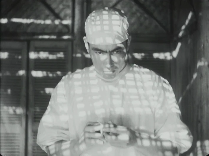 The Quiet Duel (1949) movie still: medium — An interior space with slatted walls that cast grid shadows across the room. A medical professional…