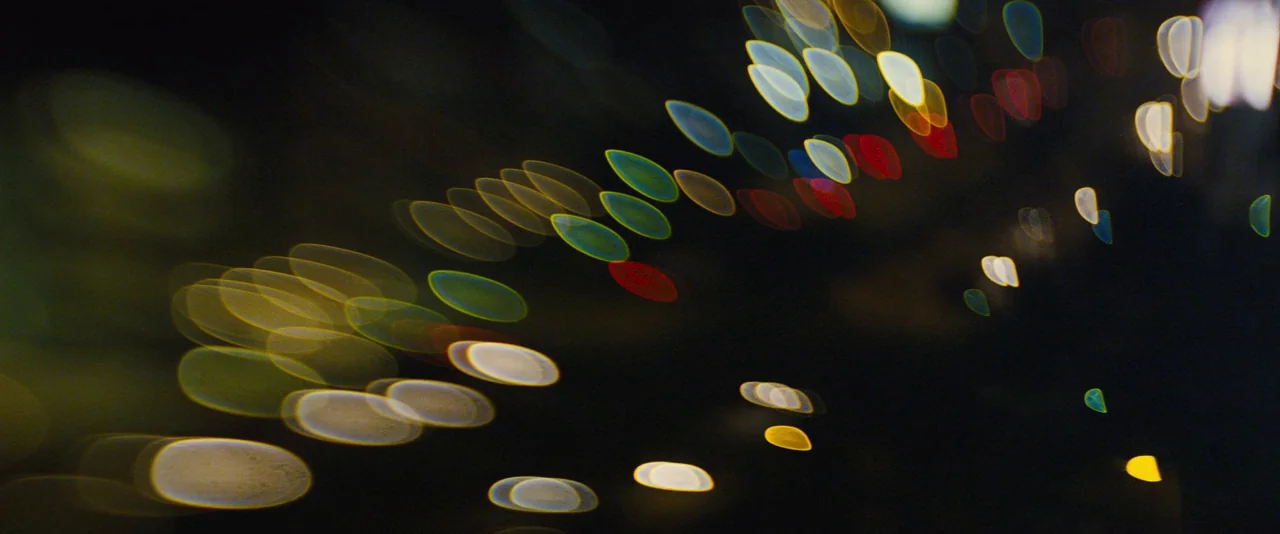 Locke (2013) movie still: establishing — A dark night scene displays numerous out-of-focus light sources across the frame. These colorful circular…