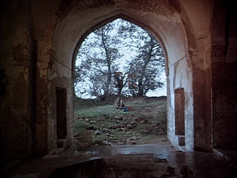 Ashik Kerib (1988) movie still: wide — An ancient stone structure features a large pointed archway leading to an outdoor landscape. A solitary…