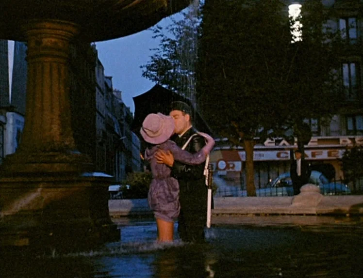 Zazie Dans Le Métro (1960) movie still: fullbody — A stone fountain sits in an urban square at night beneath dark trees. A couple in formal attire…