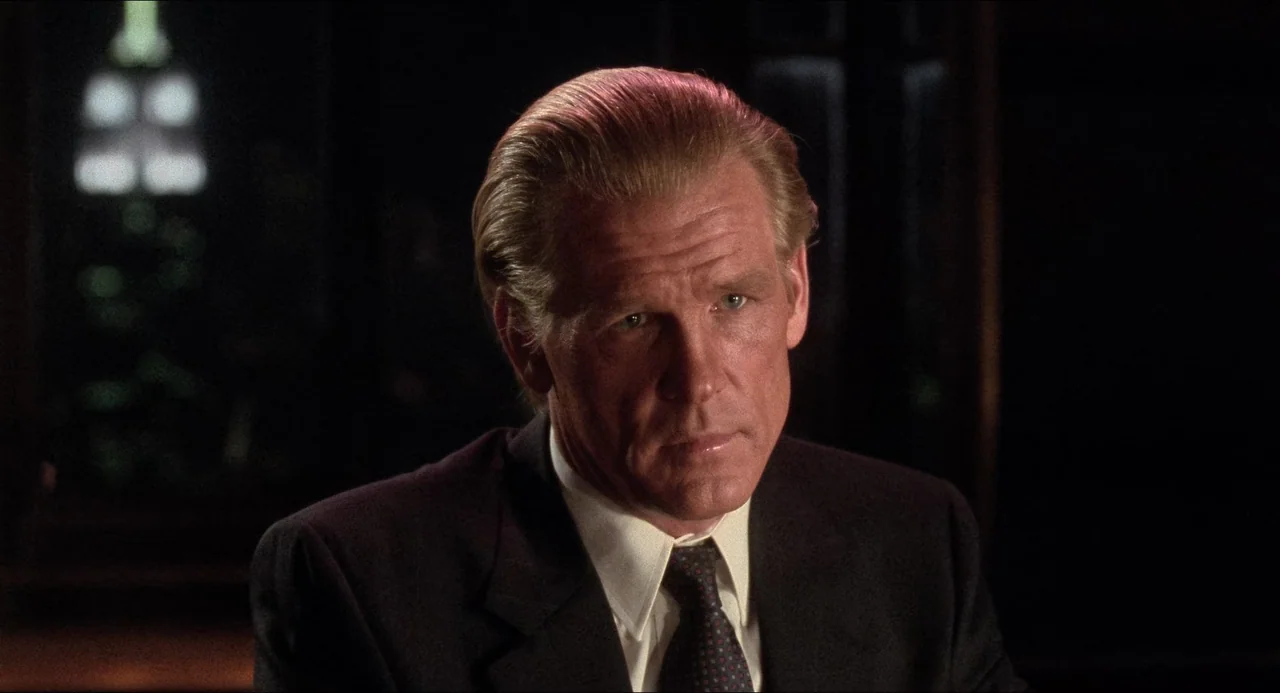 The Prince of Tides (1991) movie still: closeup — A dark office environment with blurred lights visible in the distant background. An adult man in a…