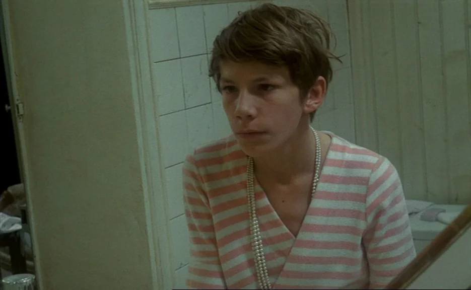 Murmur of the Heart (1971) movie still: closeup — A small room features aged, white square tiling and pale painted wall paneling. A young person in…