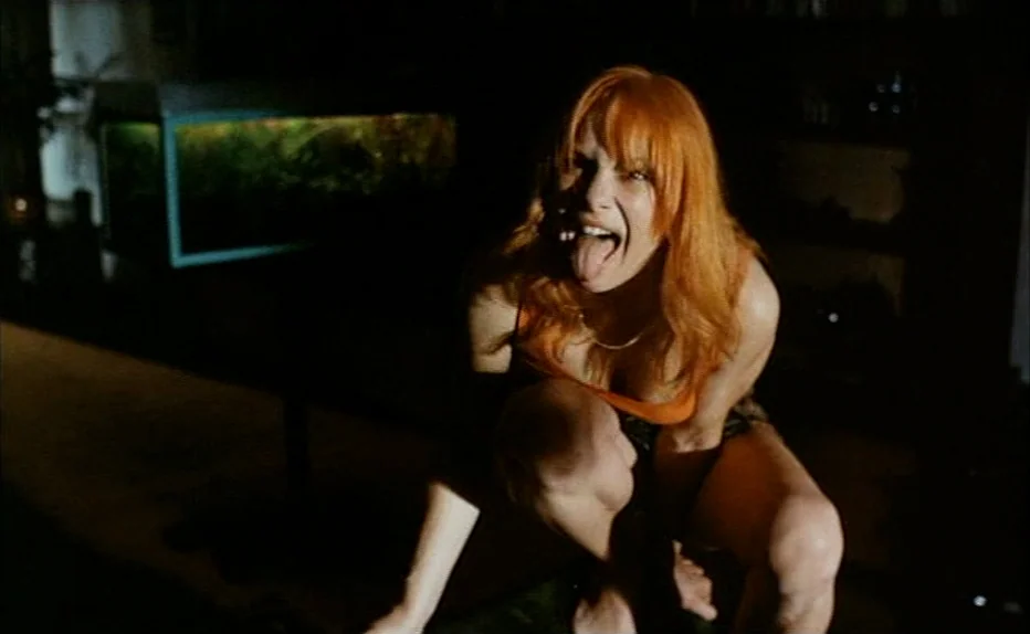 Turkish Delight (1973) movie still: medium — A dark apartment interior features a large illuminated fish tank in the background. A young woman with…