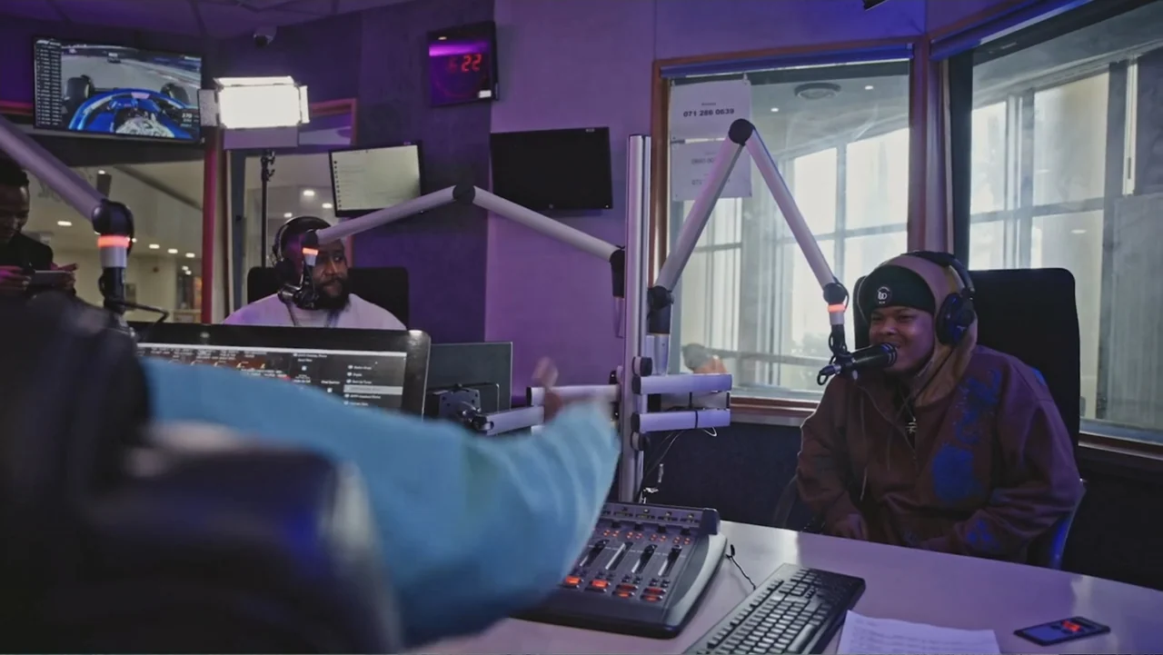 African Throne World Tour (2024) movie still: medium — A radio studio filled with technical equipment and multiple microphones on boom arms. Two men…