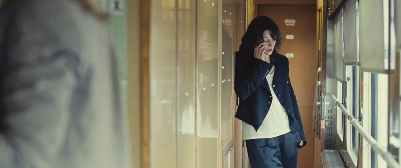 Clouds of Sils Maria (2014) movie still: medium — A narrow train corridor with wood paneling and a large window along the side. A woman in a black…