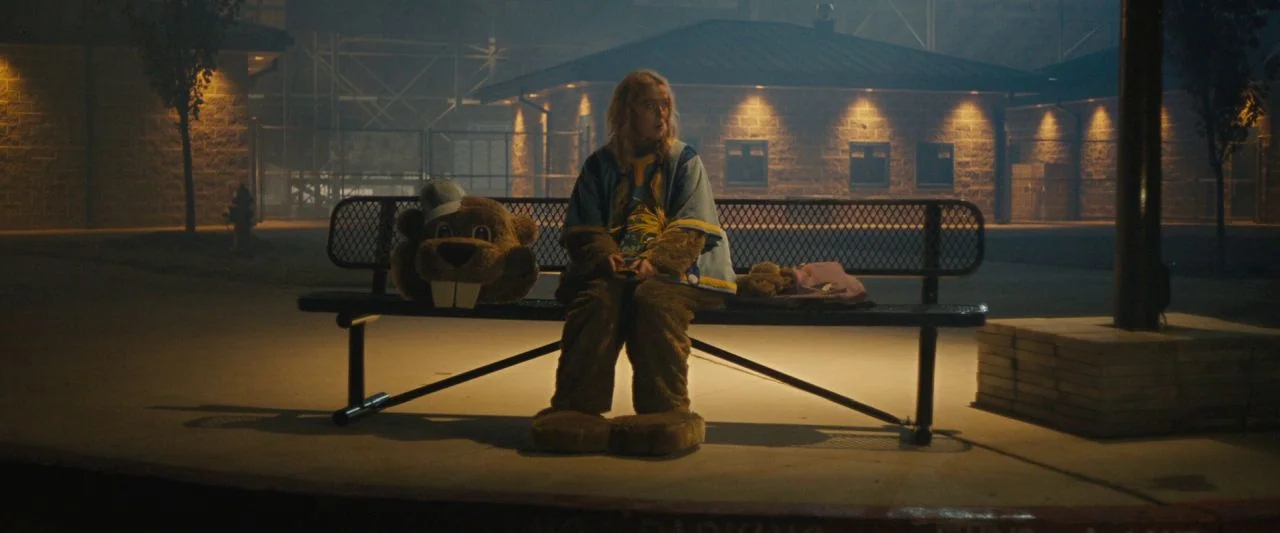 Freaky (2020) movie still: fullbody — A dark, empty paved area sits in front of a brick building at night. A young woman wearing part of a mascot…