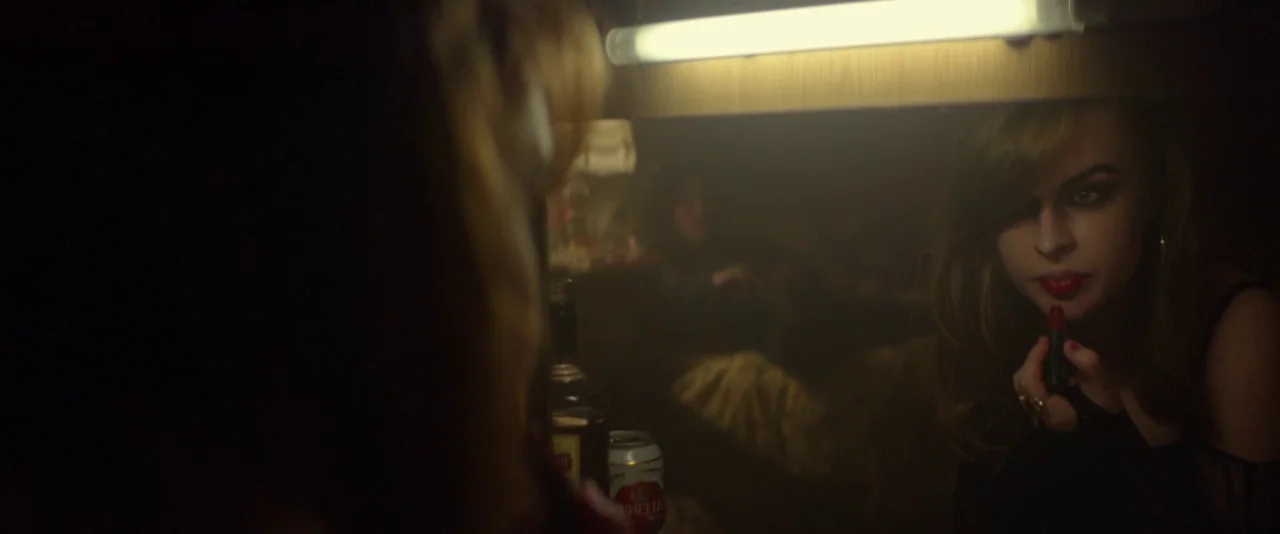 Kissing Candice (2017) movie still: closeup — A dimly lit room with a mirror reflecting a woman at a cluttered vanity. The woman focuses intently on…