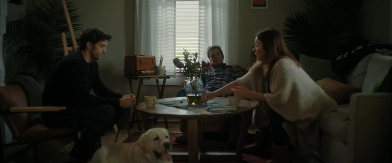 Someone Like You (2024) movie still: medium — A living room interior features a circular wooden coffee table centered between three seated adults. A…
