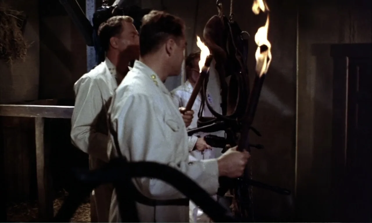 Journey to the Seventh Planet (1962) movie still: medium — A rustic barn-like interior with wooden posts and hay bundles in the shadows. Three men…