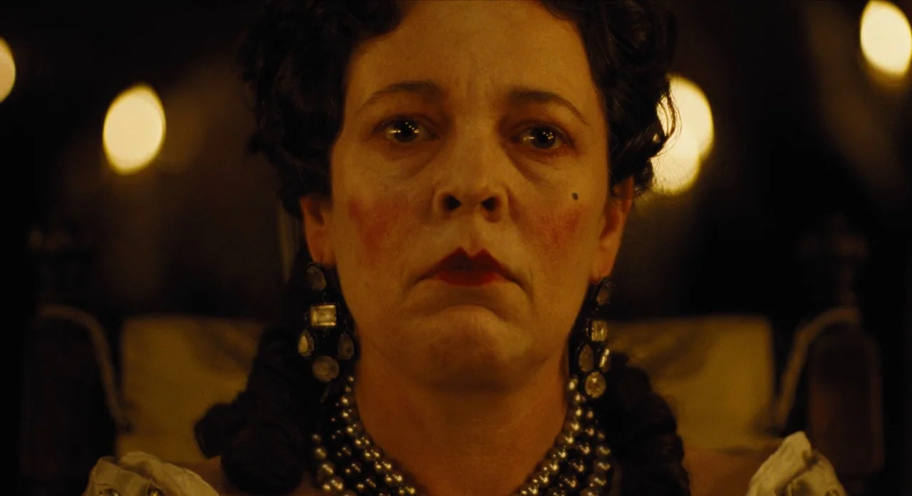 The Favourite (2018) movie still: closeup — A dimly lit room features a woman seated against an obscured dark background. The subject maintains a…