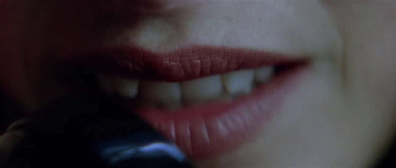 Lost Highway (1997) movie still: closeup — A close-up captures a person's mouth partially obscured by a dark object. The subject presses a phone…