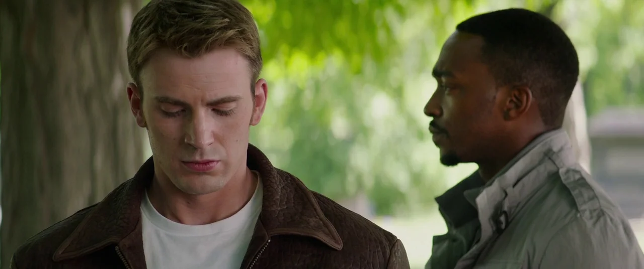 Captain America: The Winter Soldier (2014) movie still: medium — Two men stand outdoors in a park-like setting with blurred green trees in…