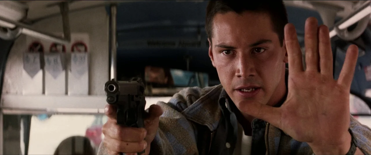 Speed (1994) movie still: closeup — Inside a public transit bus with metal bars visible in the background. A man holds a pistol forward with his…
