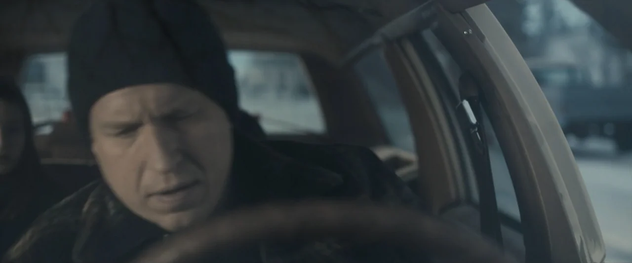The Best Christmas Pageant Ever (2024) movie still: closeup — A view inside the front seat of a car during the daytime. The driver wears a black…