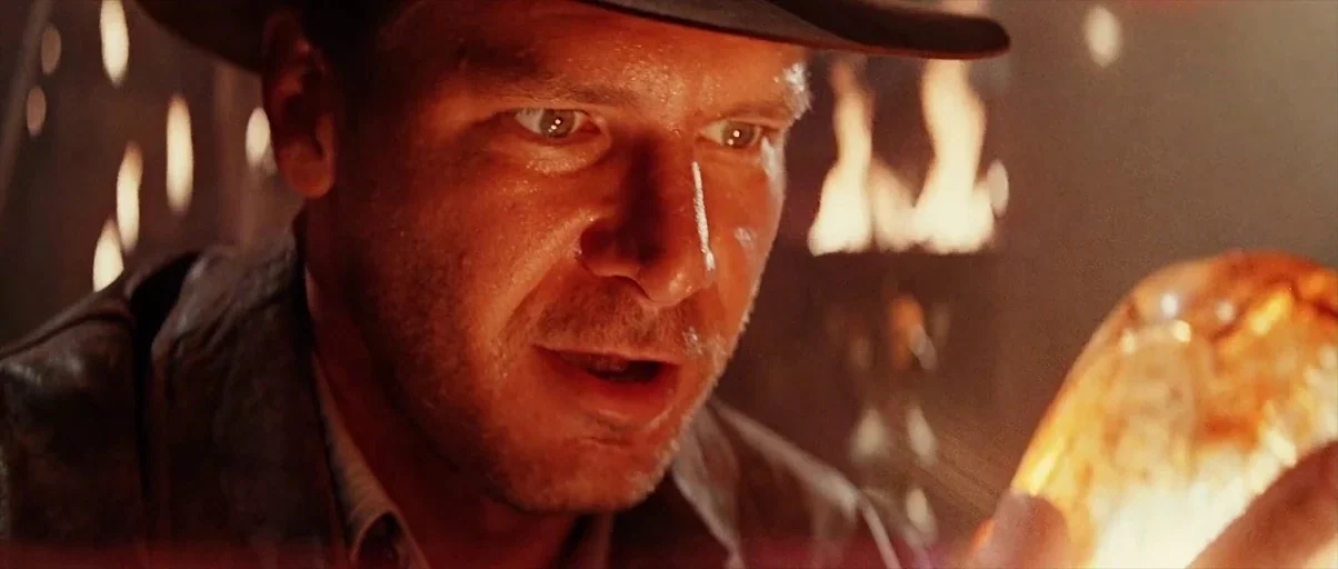 Indiana Jones and the Last Crusade (1989) movie still: closeup — The interior of a dimly lit, ancient stone space with flickering torches. A man…