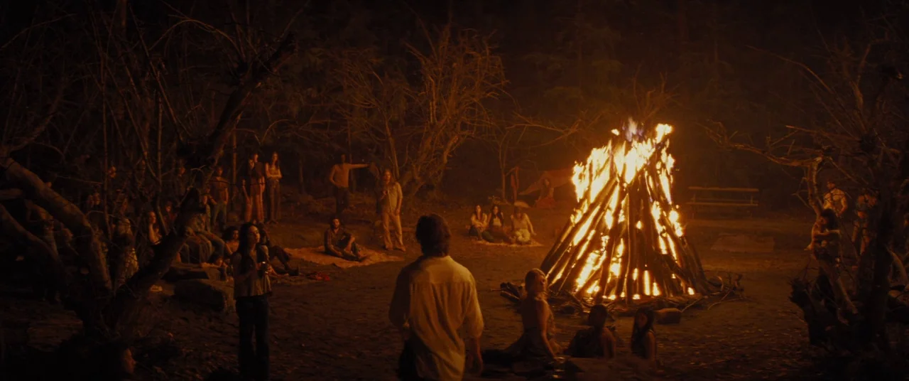 Bad Times at the El Royale (2018) movie still: wide — A clearing in a dense, dark forest features a massive, crackling bonfire at center. Multiple…