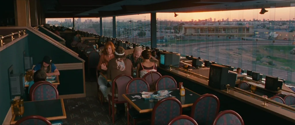 Away We Go (2009) movie still: wide — A spacious, multi-level racetrack dining area features dark green walls and patterned chairs. Patrons sit at…