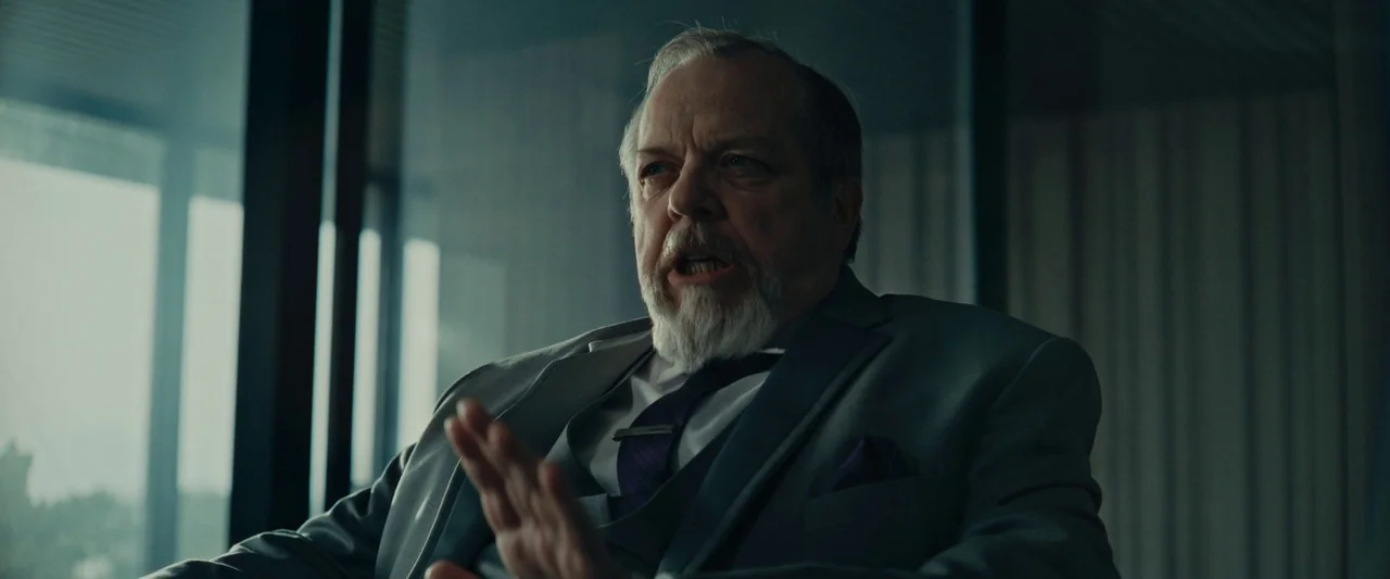 We Are Zombies (2023) movie still: medium — A modern, dimly lit space with floor-to-ceiling windows featuring vertical blinds and glass partitions.…