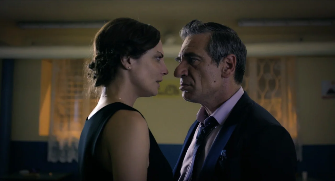 Boyka: Undisputed IV (2016) movie still: medium — A dimly lit room with yellow walls and white curtains in the background. A woman in a black dress…